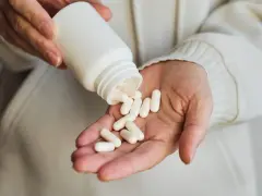Dłonie wysypują białe kapsułki z butelki na dłoń. Wśród nich widać suplement gaba.