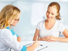 Lekarka w białym kitlu notuje coś na kartce, pacjentka uśmiecha się, zastanawiając się, htz co to za badanie.